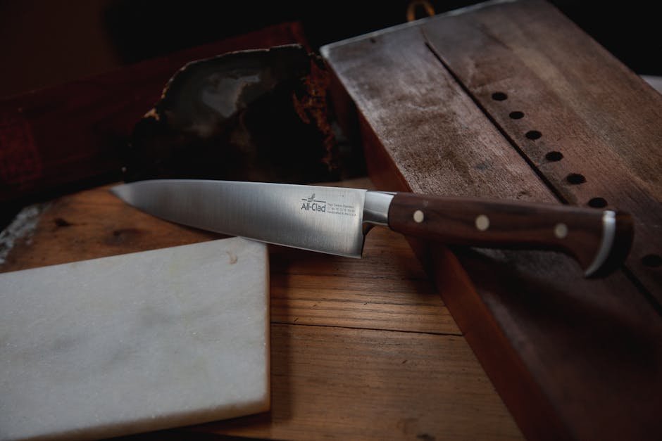 A sharp steel kitchen knife with wooden handle on a rustic table.